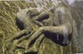 kuvassa kivinen veistos, jossa kaksi ihmishahmoa sylikkäin käpertyneenä sikiöasentoon järven rannassa veden alla