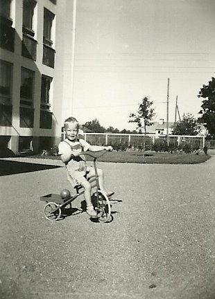 kuvassa pieni poika ajaa kolmipyöräisellä kerrostalon pihalla