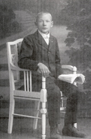 valokuva jossa pieni poika istuu tuolilla tumma puku päällä