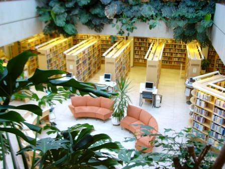 kuvassa näkymä kirjastosaliin jossa kirjahyllyjen ympäröimänä kaksi vaaleanpunertavaa kaarenmuotoista sohvaa