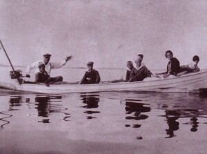 valokuva soutuveneestä, joss hattupäinen mies vilkuttaa kyydissä myös lapsia ja naisia