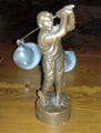 kuvassa pieni patsas, jossa ihmihahmo kantaa kahta lasista sankoa kepin päässä